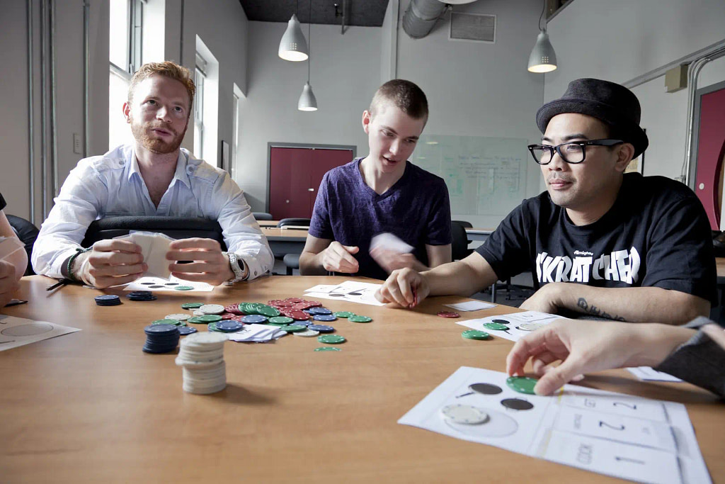 A Group Of People Sitting Around A Table Playing A Game With Poker Chips.