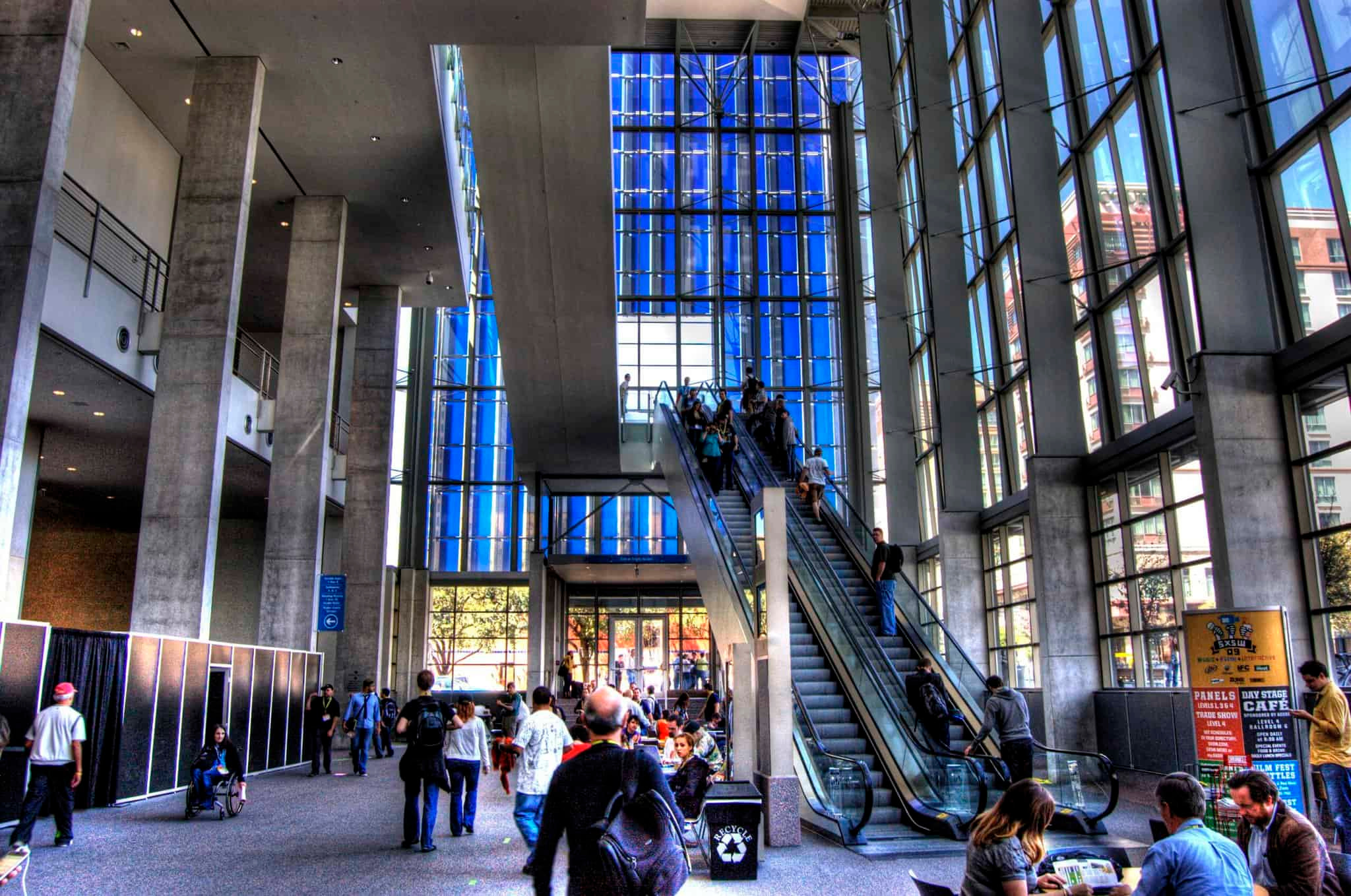 Austin Convention Center Interior – Sun‑Lit Glass Atrium With Escalators, Concrete Columns And Attendees Arriving