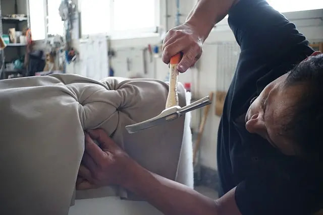 A Worker Attaches Cloth To A Piece Of Furniture Using A Hammer. 