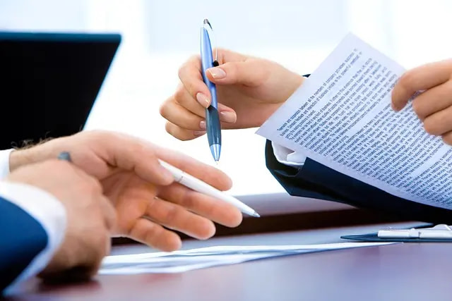 Two People's Hands Holding Pens Near Some Documents.