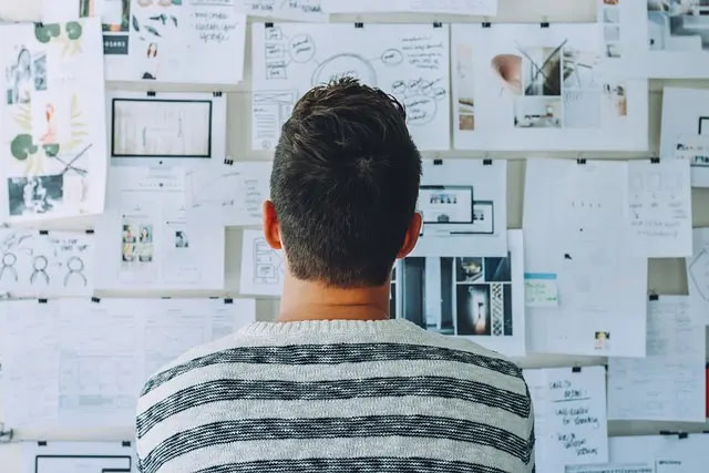 A man looks at his planning pin board full of diagrams and notes.
