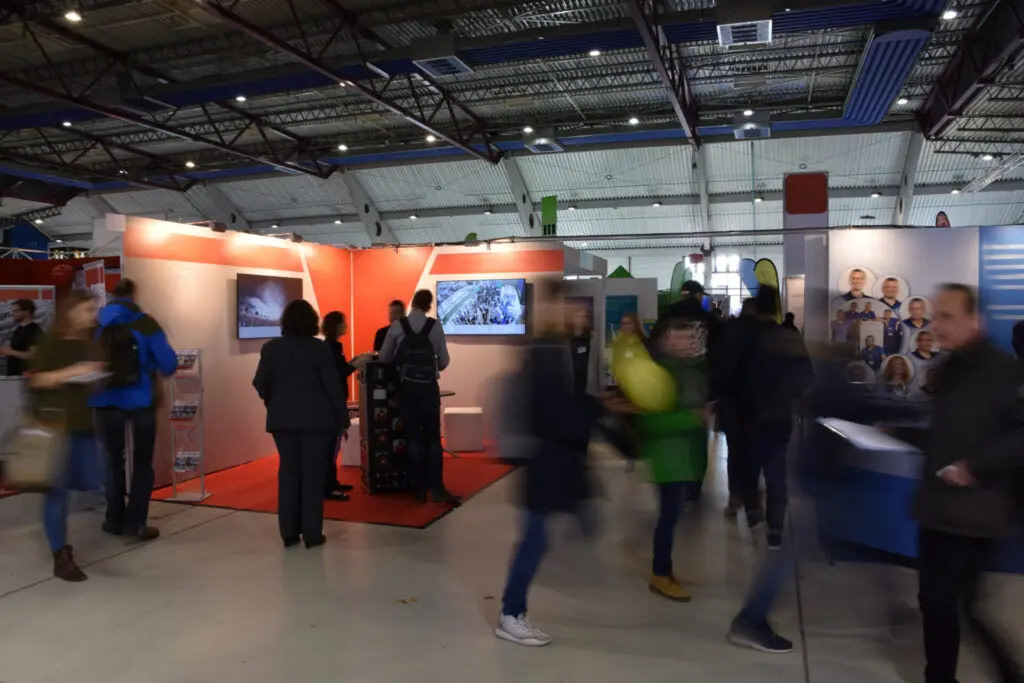 A Blurred Shot Of Visitors Passing By At An Indoor Trade Show.